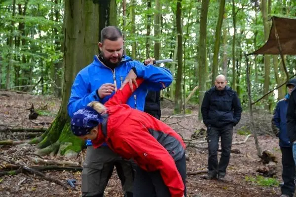 Person zeigt einer anderen Person eine Technik im Wald