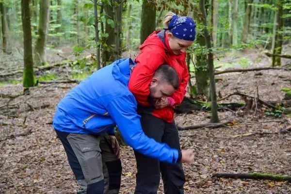 Person zeigt einer anderen Person eine Technik im Wald