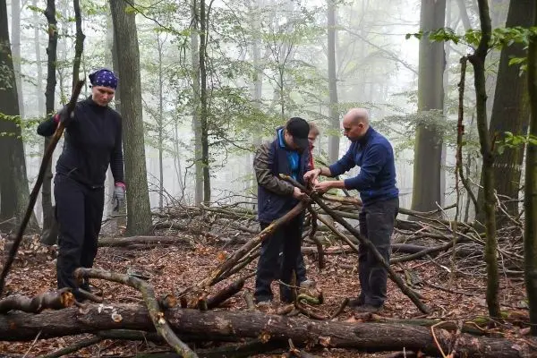 Vier Personen bauen eine selbstgebaute Konstruktion aus Ästen im Wald