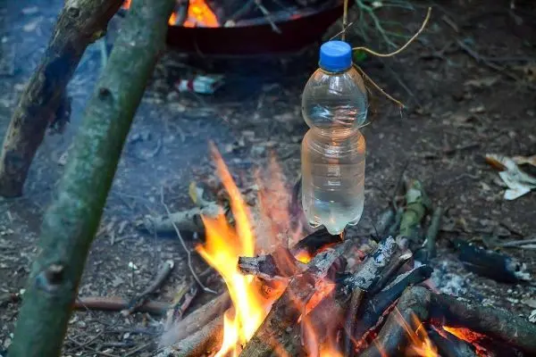 Wasserflasche hängt über einem brennenden Holzstapel