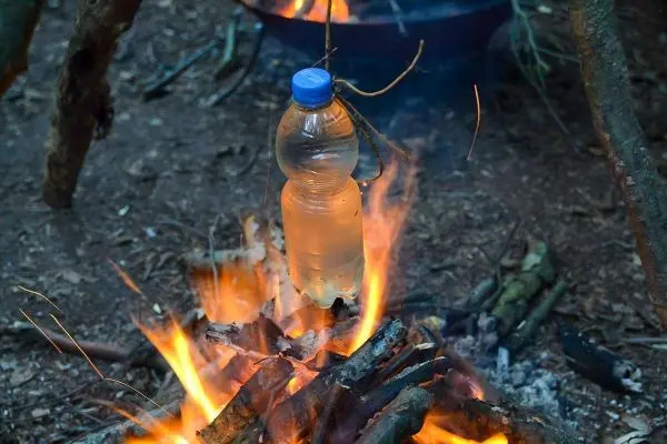 Wasserflasche hängt über einem kleinen Feuer aus Holz