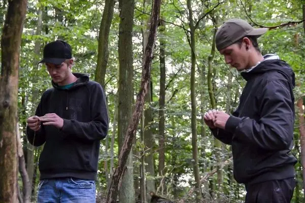 Zwei Personen arbeiten konzentriert mit Schnüren im Wald