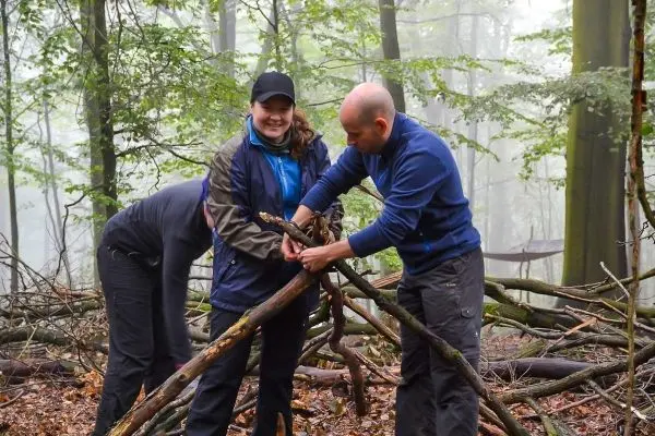 Zwei Personen bauen eine Holzstruktur im Wald aus Ästen