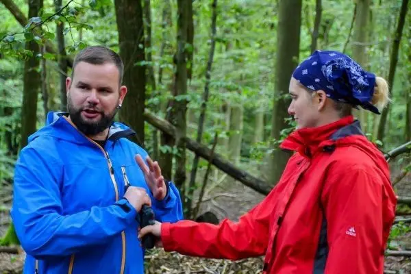 Zwei Personen im Wald, eine Person zeigt mit der Hand auf ein Objekt