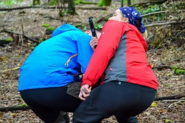 Zwei Personen in Outdoor-Bekleidung üben eine Nahkampfsituation im Wald
