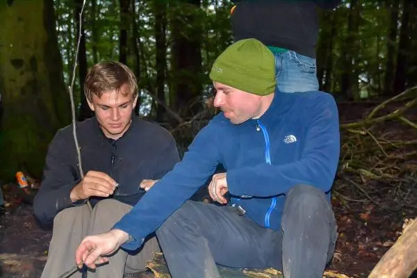 Zwei Personen sitzen im Wald und arbeiten an einem Feuerzeug