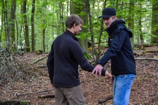 Zwei Personen stehen im Wald und führen eine Handbewegung aus