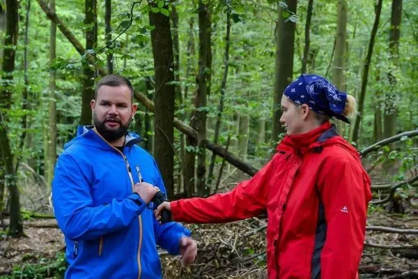 Zwei Personen stehen im Wald und interagieren miteinander