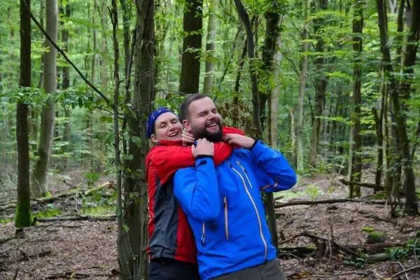 Zwei Personen stehen in einem Wald und umarmen sich spielerisch
