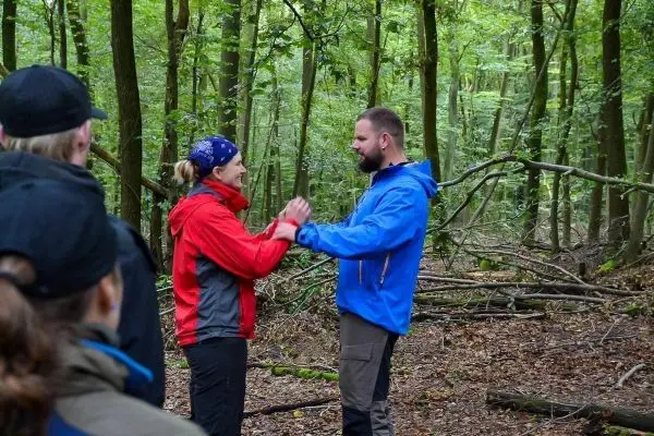 Zwei Personen üben eine Interaktion im Wald, umgeben von Bäumen und Ästen