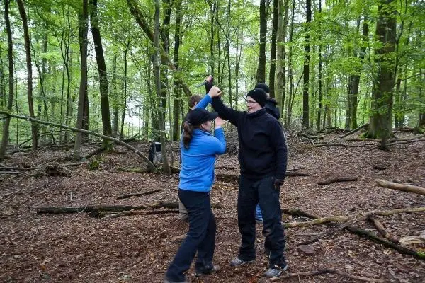 Zwei Personen üben eine Technik im Wald, Hände sind erhoben