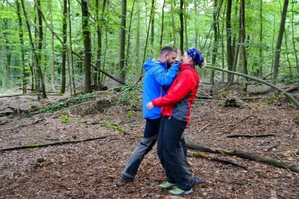 Zwei Personen üben eine Technik in einem Waldgebiet mit Laub und Bäumen