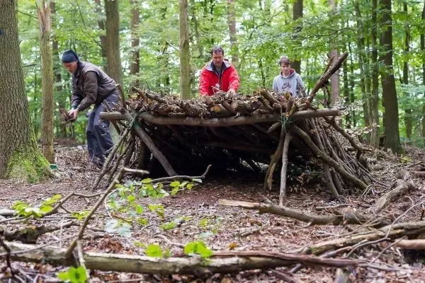 Drei Personen bauen eine improvisierte Notunterkunft aus Ästen und Laub
