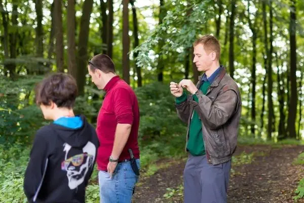 Drei Personen stehen auf einem Waldweg und betrachten etwas in der Hand