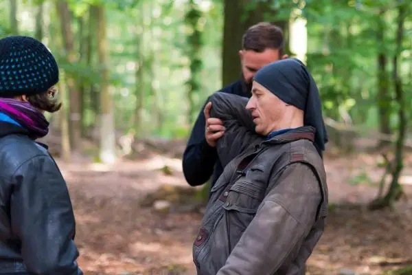 Drei Personen stehen im Wald und interagieren miteinander