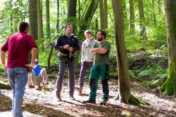 Gruppe diskutiert an einer selbstgebauten Seilbrücke im Wald