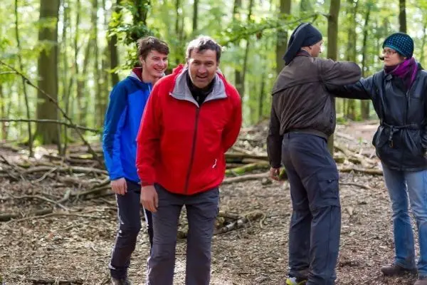 Gruppe im Wald steht zwischen Bäumen und Ästen, eine Person berührt eine andere