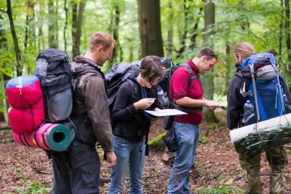 Gruppe mit Rucksäcken schaut auf Karte im Wald beim Überlebenstraining