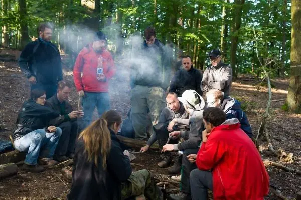 Gruppe sitzt um ein kleines Bodenfeuer, Rauch steigt auf