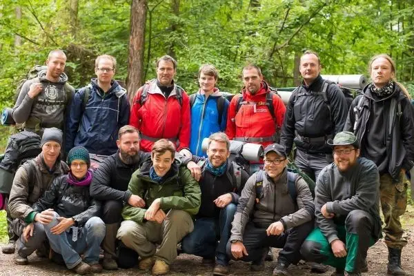 Gruppe von Personen posiert im Wald mit Rucksäcken beim Überlebenstraining