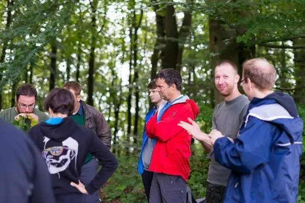 Gruppe von Personen steht im Wald und diskutiert miteinander
