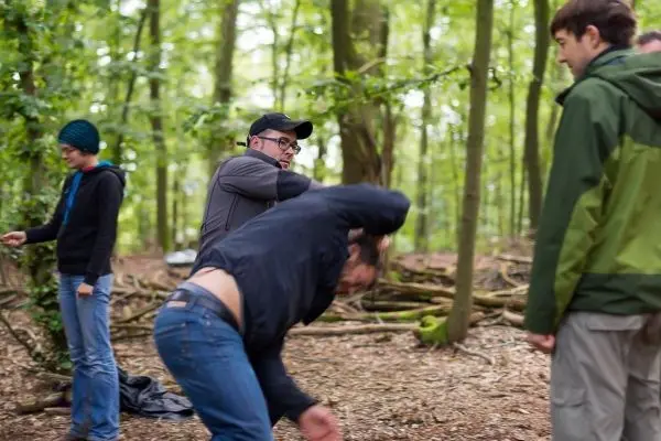Gruppenteilnehmer üben eine Technik im Wald, einer beugt sich nach vorne