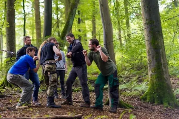 Gruppierung von Personen bei einer Seilquerung im Wald, Seil zwischen Bäumen gespannt