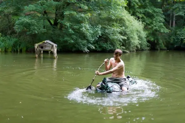 Junge paddelt mit improvisiertem Boot auf einem ruhigen Gewässer