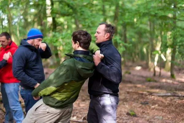 Kampftraining mit mehreren Personen im Wald, einer greift einen anderen an