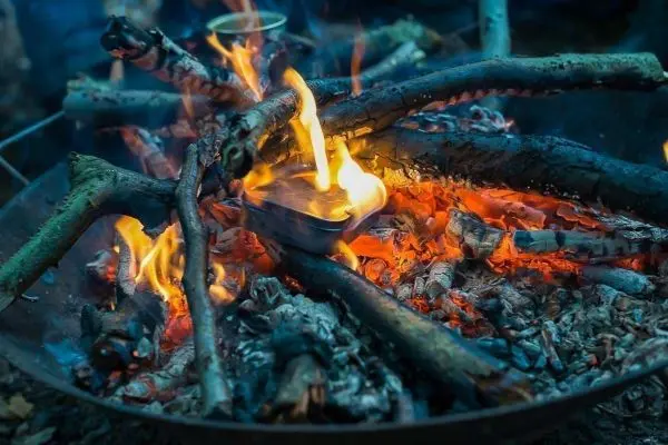 Kleine Flamme brennt in einer Metalldose auf einem Holzfeuer