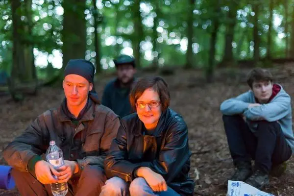 Lagerfeuer in einem Wald mit mehreren Personen, eine hält eine Wasserflasche