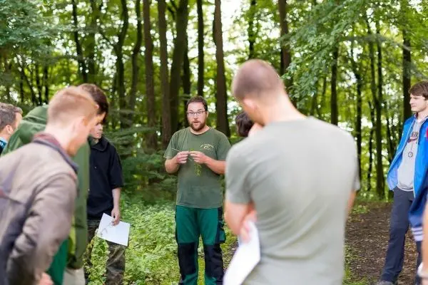 Mann erklärt einer Gruppe von Teilnehmern etwas im Wald