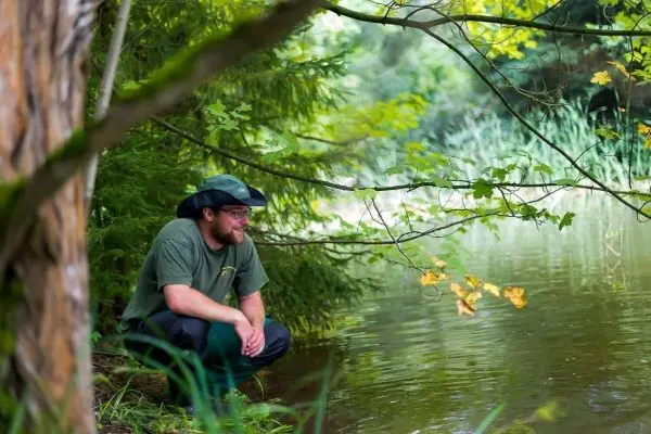 Mann hockt am Ufer eines Gewässers und beobachtet das Wasser