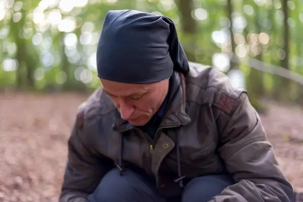 Mann kniet im Wald und konzentriert sich auf den Boden