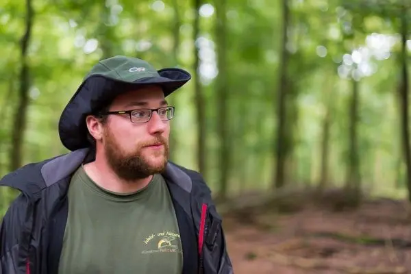 Mann mit Brille und Hut steht im Wald
