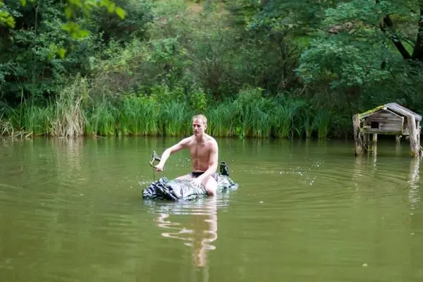 Mann paddelt auf improvisiertem Floß in einem Gewässer