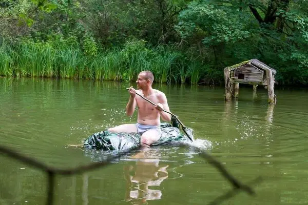 Mann paddelt auf improvisiertem Floß in einem Gewässer