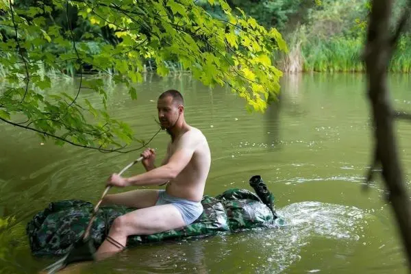 Mann paddelt in einem camouflagefarbenen Schlauchboot auf einem ruhigen Gewässer