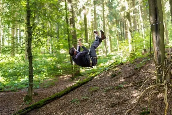 Mann überquert selbstgebaute Seilbrücke zwischen Bäumen im Wald
