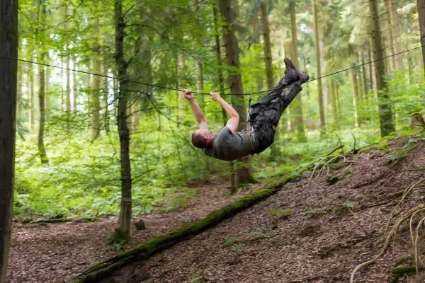 Mann überquert selbstgebaute Seilbrücke zwischen Bäumen im Wald