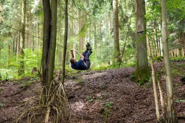 Mann überquert selbstgebaute Seilbrücke zwischen Bäumen im Wald