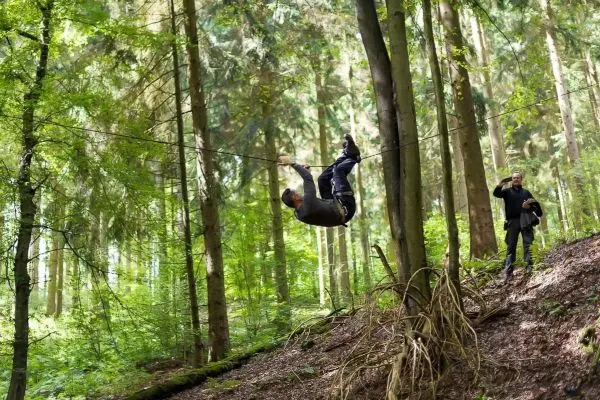Mann überquert selbstgebaute Seilbrücke zwischen Bäumen im Wald