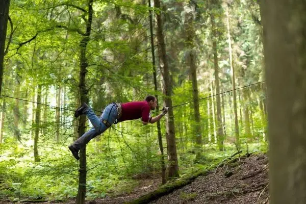 Mann überquert selbstgebaute Seilbrücke zwischen zwei Bäumen