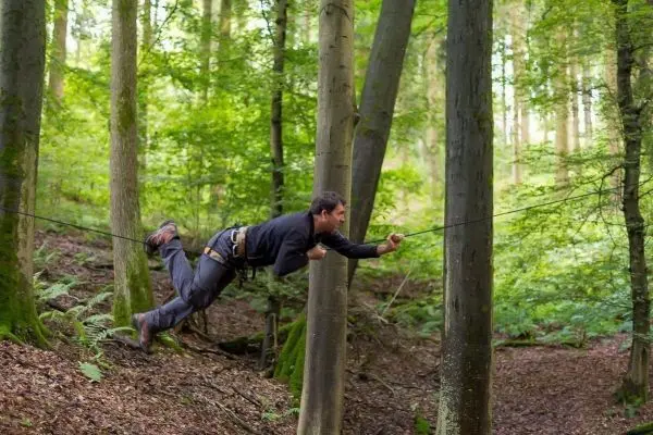Mann überquert selbstgebaute Seilbrücke zwischen zwei Bäumen im Wald