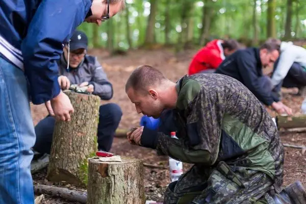 Messer schneidet Zunder auf einem Baumstumpf, während Teilnehmer umherarbeiten