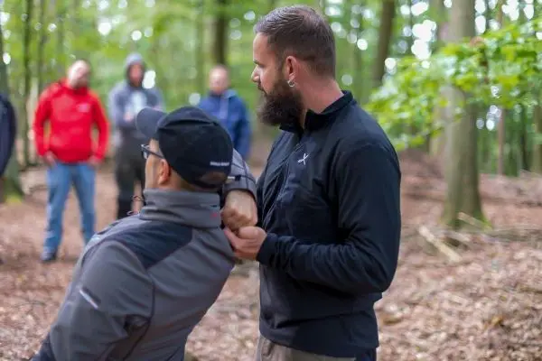 Person demonstriert eine Technik an einer anderen Person im Wald