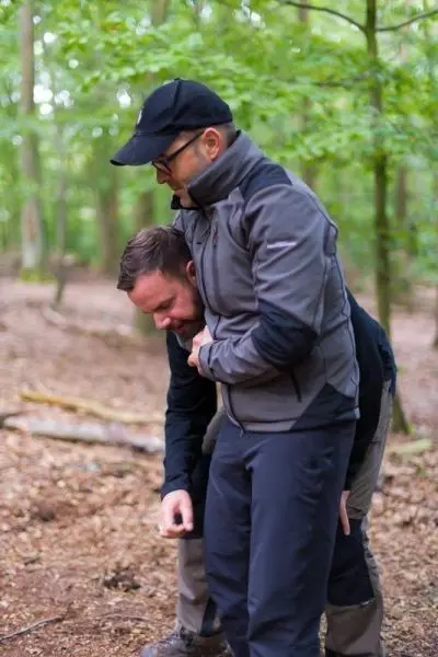 Person hilft anderer Person beim Anlegen einer Ausrüstung im Wald