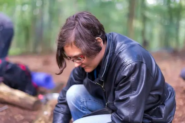 Person kniet sich auf den Boden und bearbeitet Holzstücke im Wald