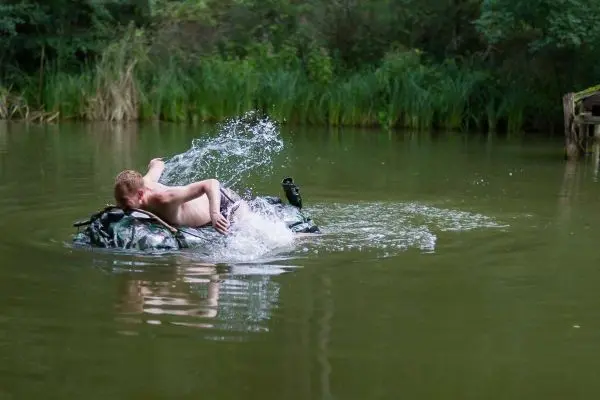Person paddelt auf einem camouflagefarbenen Schwimmkörper im Wasser