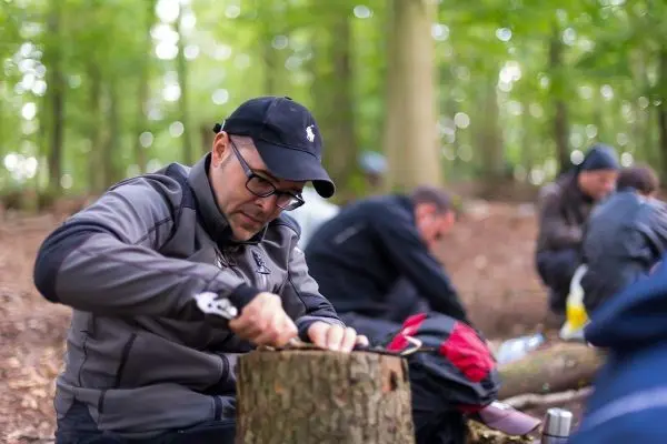 Person schnitzt an einem Holzstück im Wald beim Survival Training